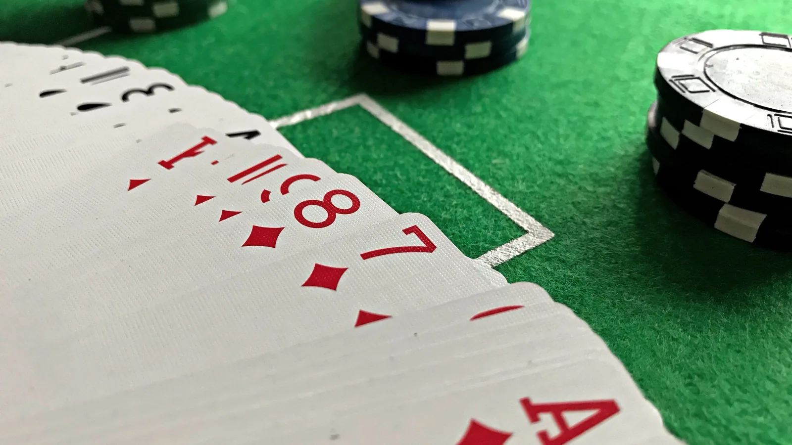 A fanned hand of playing cards showing an ace of diamonds next to stacks of black and white poker chips on a green felt table