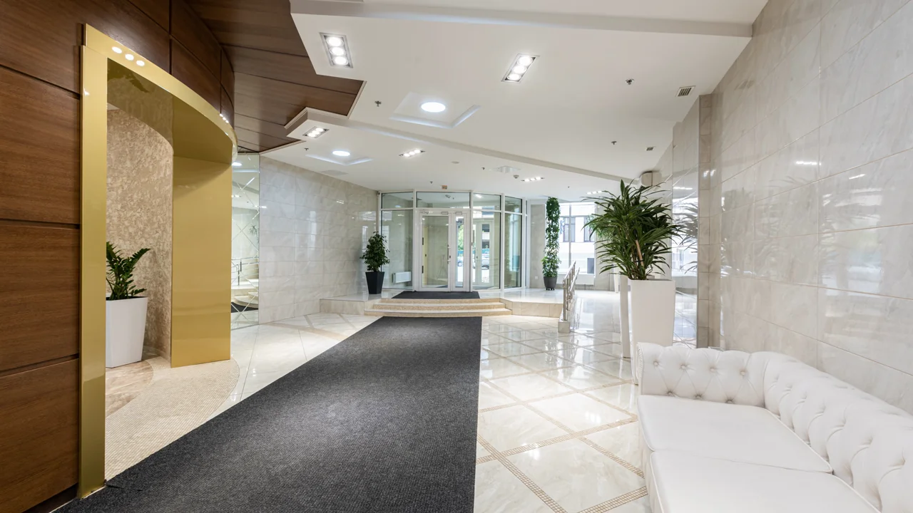 A modern luxury hotel lobby entrance with polished marble floors, a gold accent column, and a plush white tufted sofa
